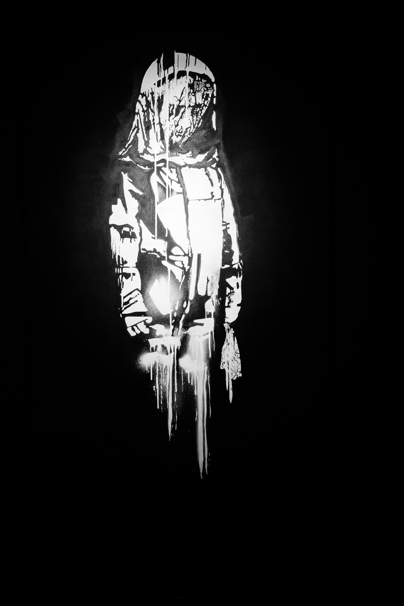 The image features a striking black-and-white mural of an astronaut, depicted with bold, dripping paint that creates a sense of motion and depth. The astronaut stands centrally against a completely black background, which enhances the stark contrast of the white paint. The figure appears contemplative, holding a light, possibly suggesting exploration or discovery. The drips of paint add an artistic flair, contributing to the overall atmosphere of intrigue and mystery.